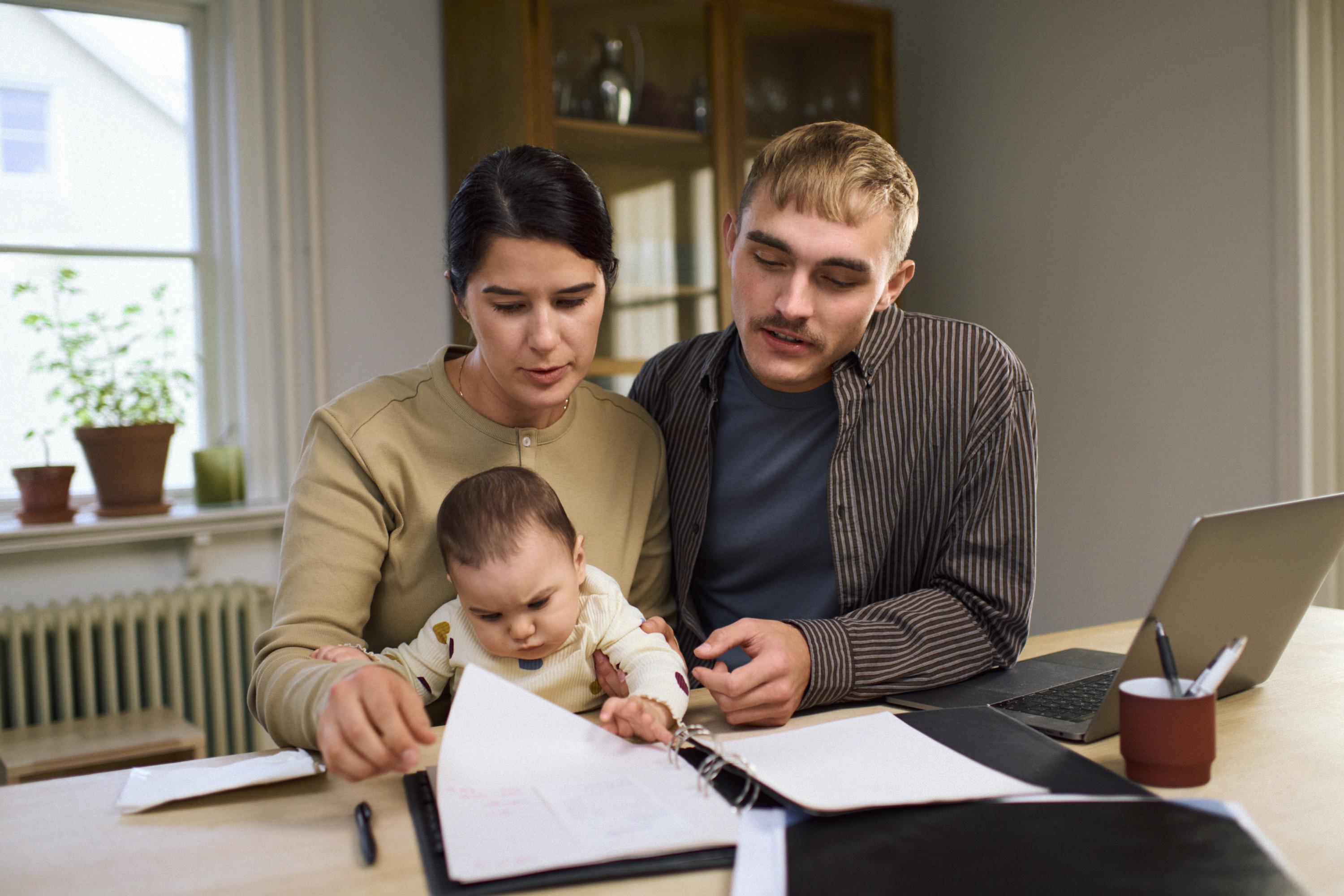 En kvinna och en man med en bebis sitter vid ett bord och tittar i en pärm.