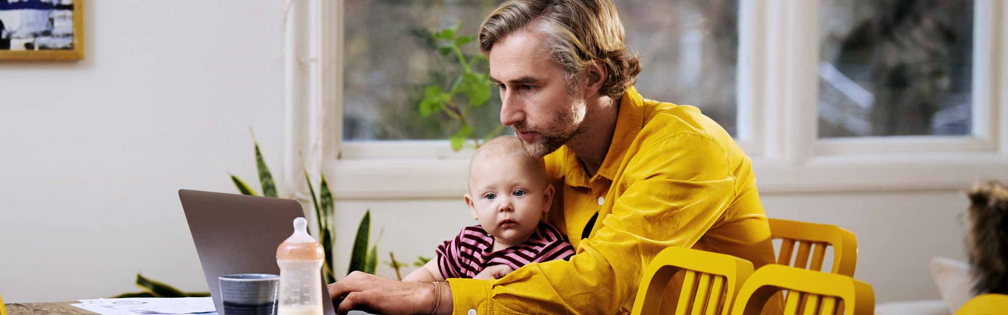 En pappa skriver på datorn med en bebis i knät