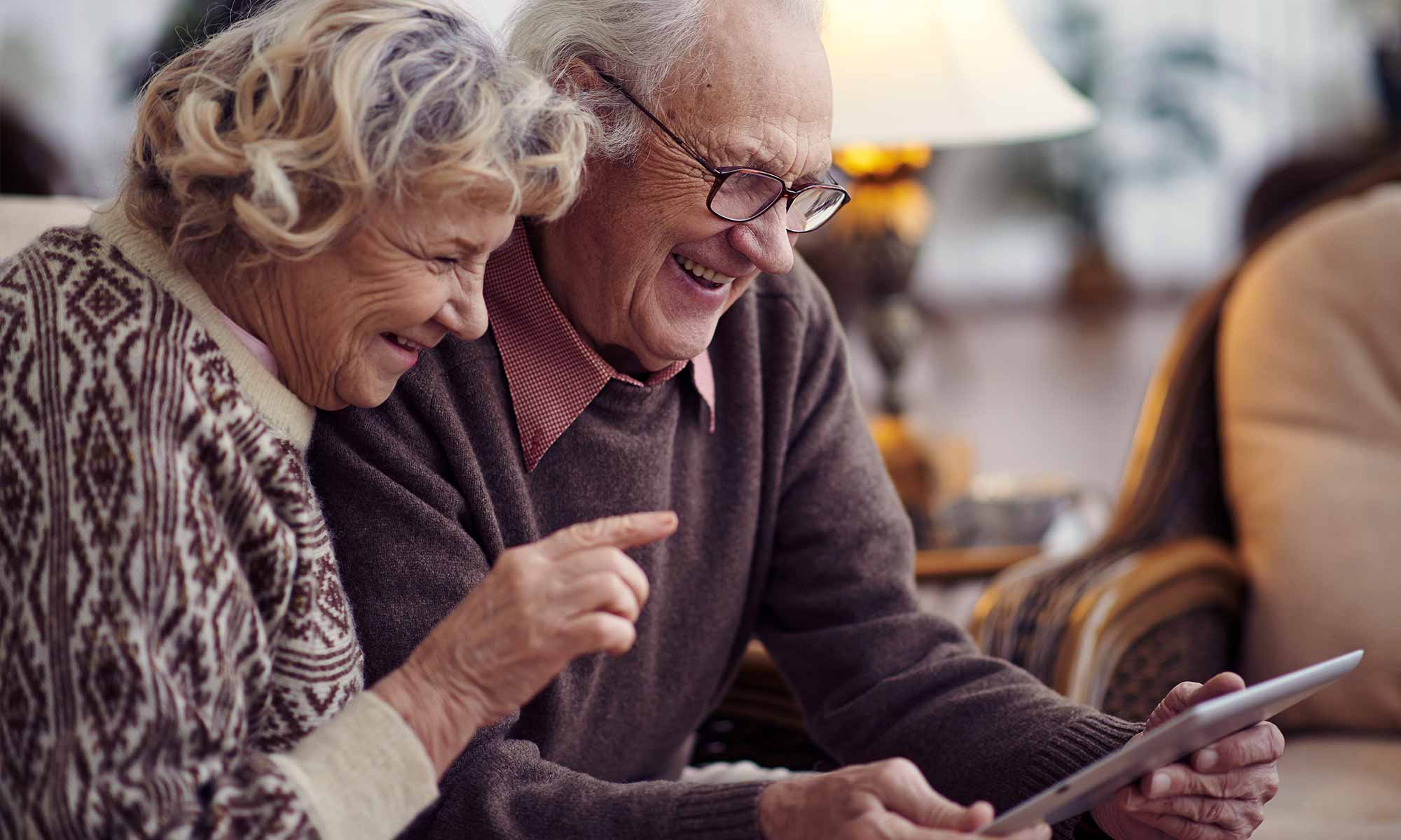 Leende äldre par sitter i en soffa och tittar på en iPad
